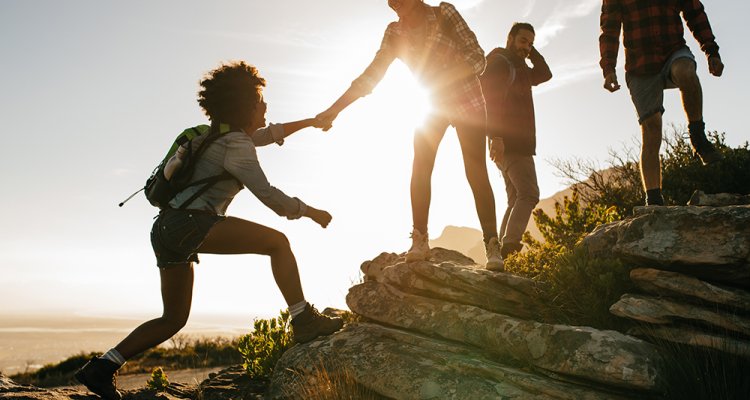 Young people helping eachother climb a mountain 