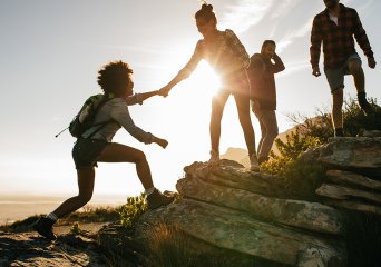 Young people helping eachother climb a mountain 