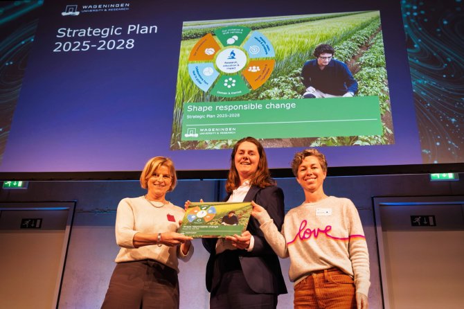 WUR-bestuursvoorzitter Sjoukje Heimovaara reikt het Strategisch Plan 2025 - 2028 uit aan Blair van Pelt van de WUR Council en Hanna Elsinga van de Student Council