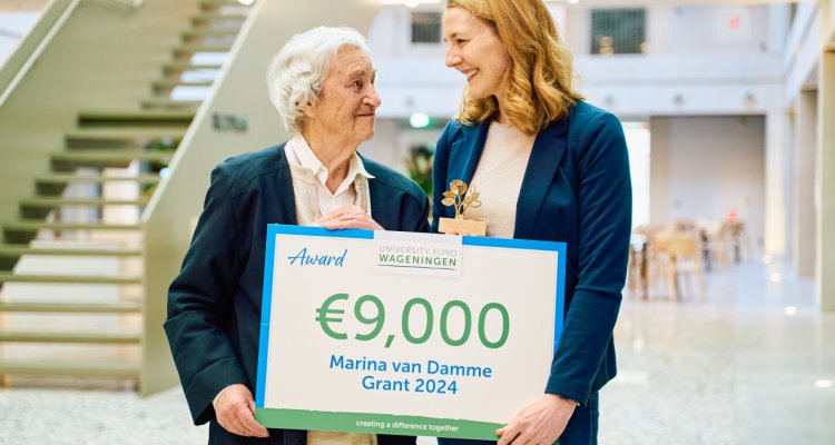 Marina van Damme en winnares Gesine Harms houden cheque vast en kijken elkaar aan